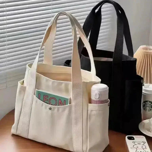 White tote bag with a black bag and Starbucks cup on a table.